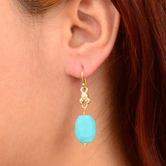 Close-up of an ear wearing a turquoise earring with gold hook.
