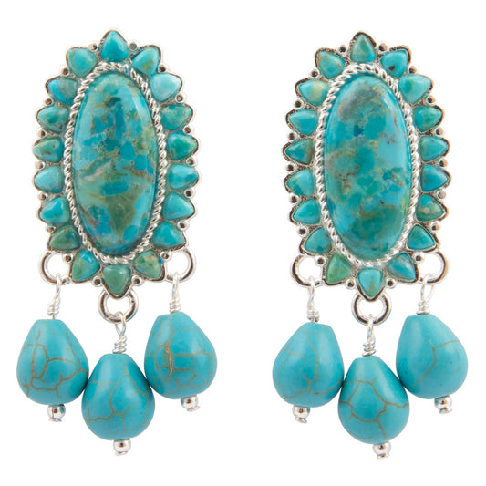 A pair of turquoise and silver dangle earrings with oval center stones surrounded by small turquoise stones, with three teardrop-shaped turquoise beads hanging below, shown on a plain white background.