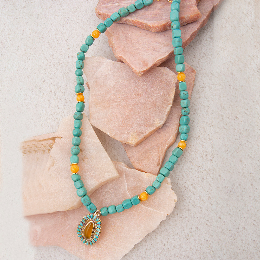 Necklace with turquoise beads and a yellow pendant on a stone surface