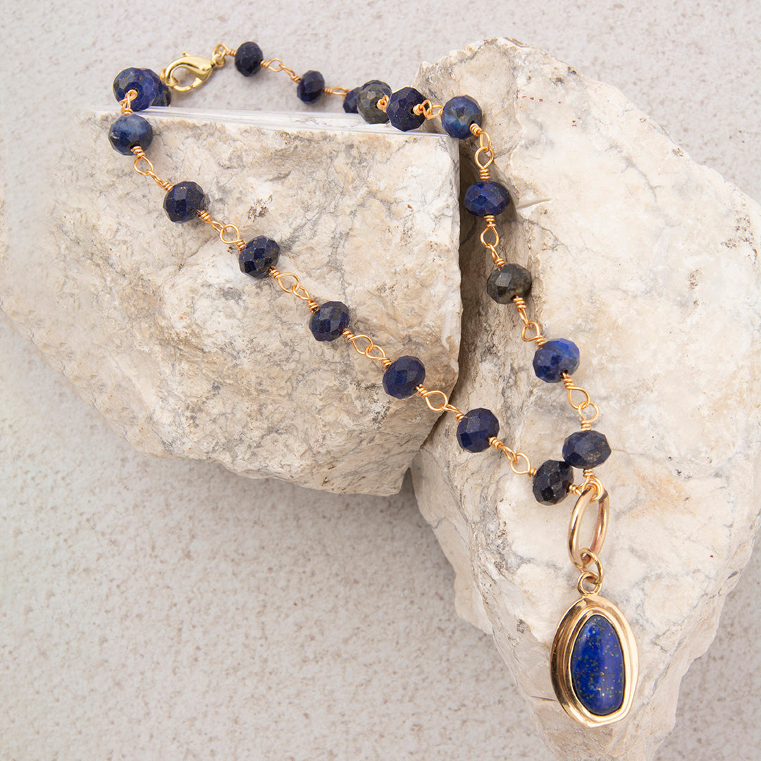 Necklace with blue beads and a gold pendant on a stone surface