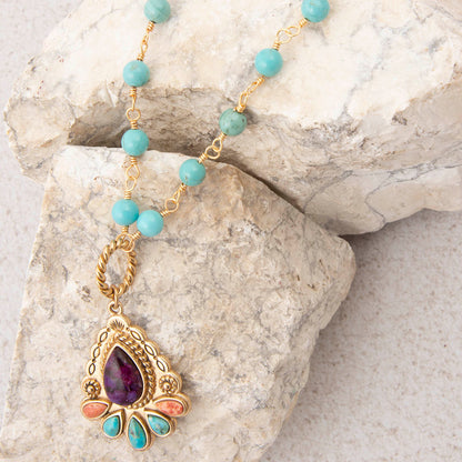 Necklace with turquoise beads and a gold pendant on a stone surface
