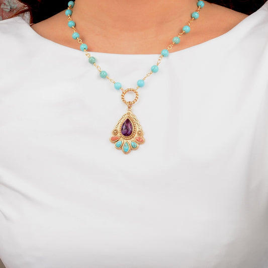 Necklace with turquoise beads and a gold pendant with a purple gemstone on a white background