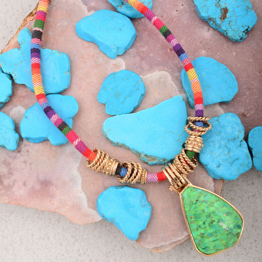 Necklace with colorful cord and green pendant on a stone surface