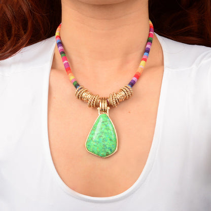 Necklace with a green pendant and colorful beaded chain worn by a person.