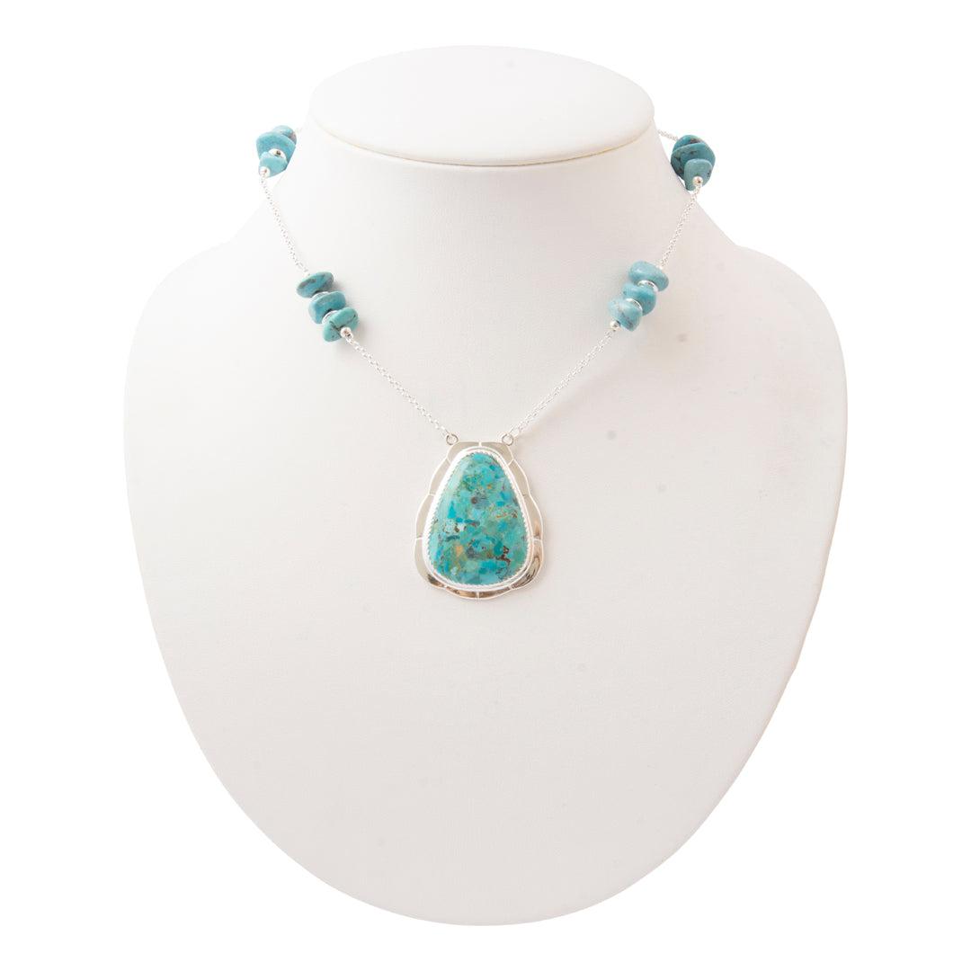 A turquoise beaded necklace with a large teardrop-shaped turquoise pendant in a silver bezel setting, displayed on a white jewelry bust.
