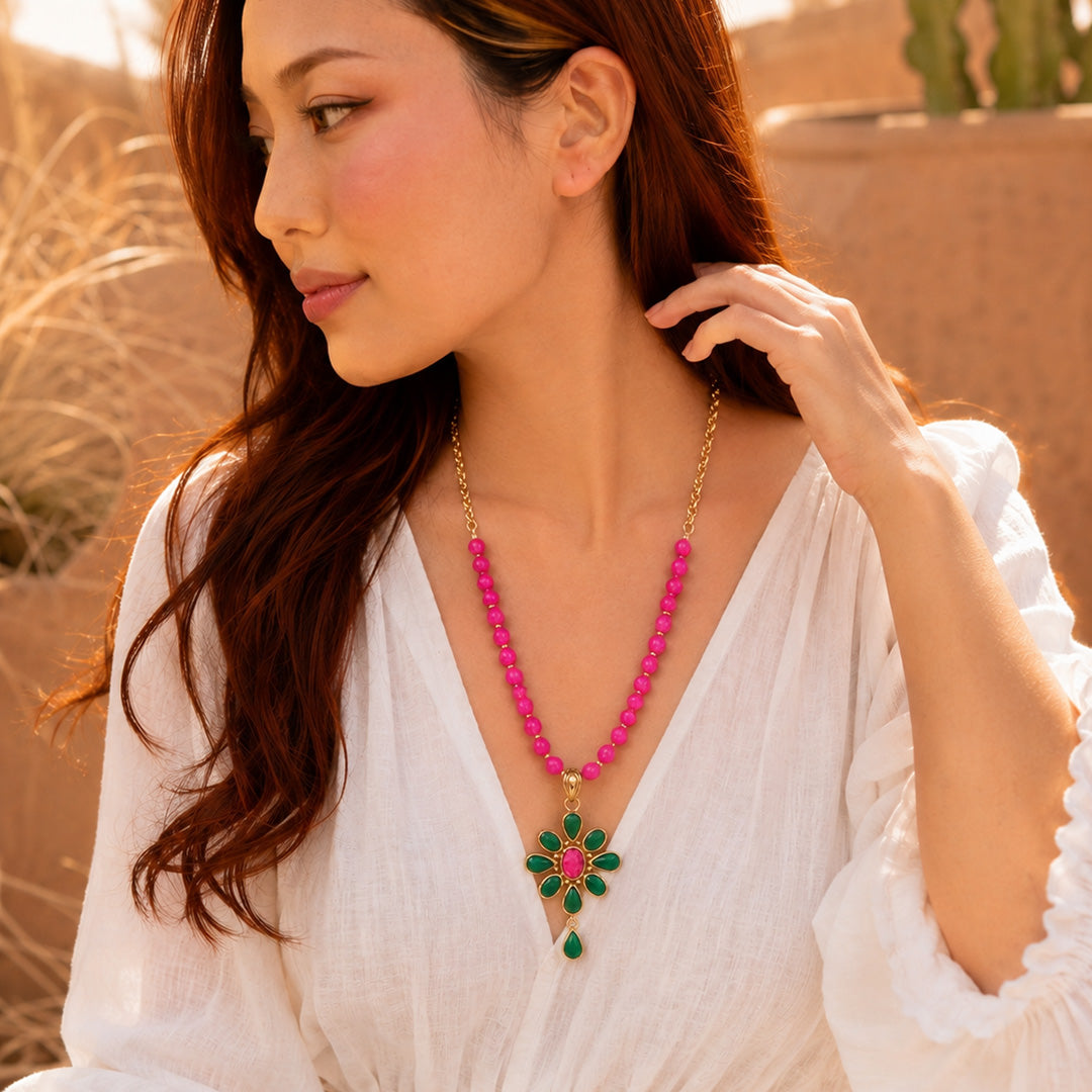 Woman wearing a pink beaded necklace with a green pendant outdoors.