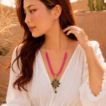 Woman wearing a pink beaded necklace with a green pendant outdoors.