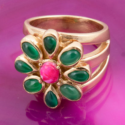 Gold ring with green gemstones and a pink center on a purple background
