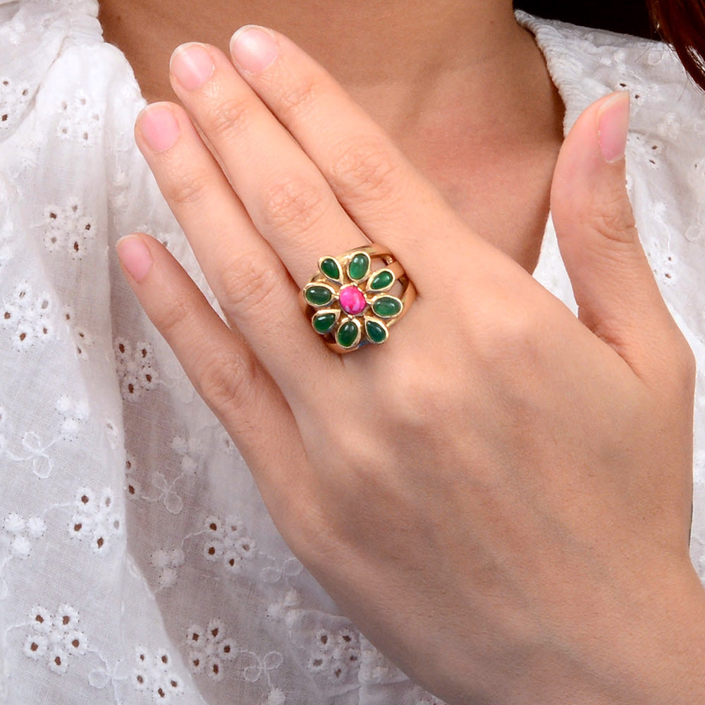 Hand wearing a decorative ring with green and pink stones against a white lace background