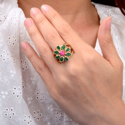 Hand wearing a decorative ring with green and pink stones against a white lace background