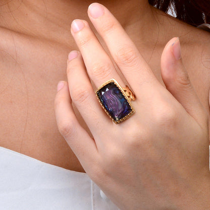 Hand wearing a gold ring with a purple gemstone on a neutral background