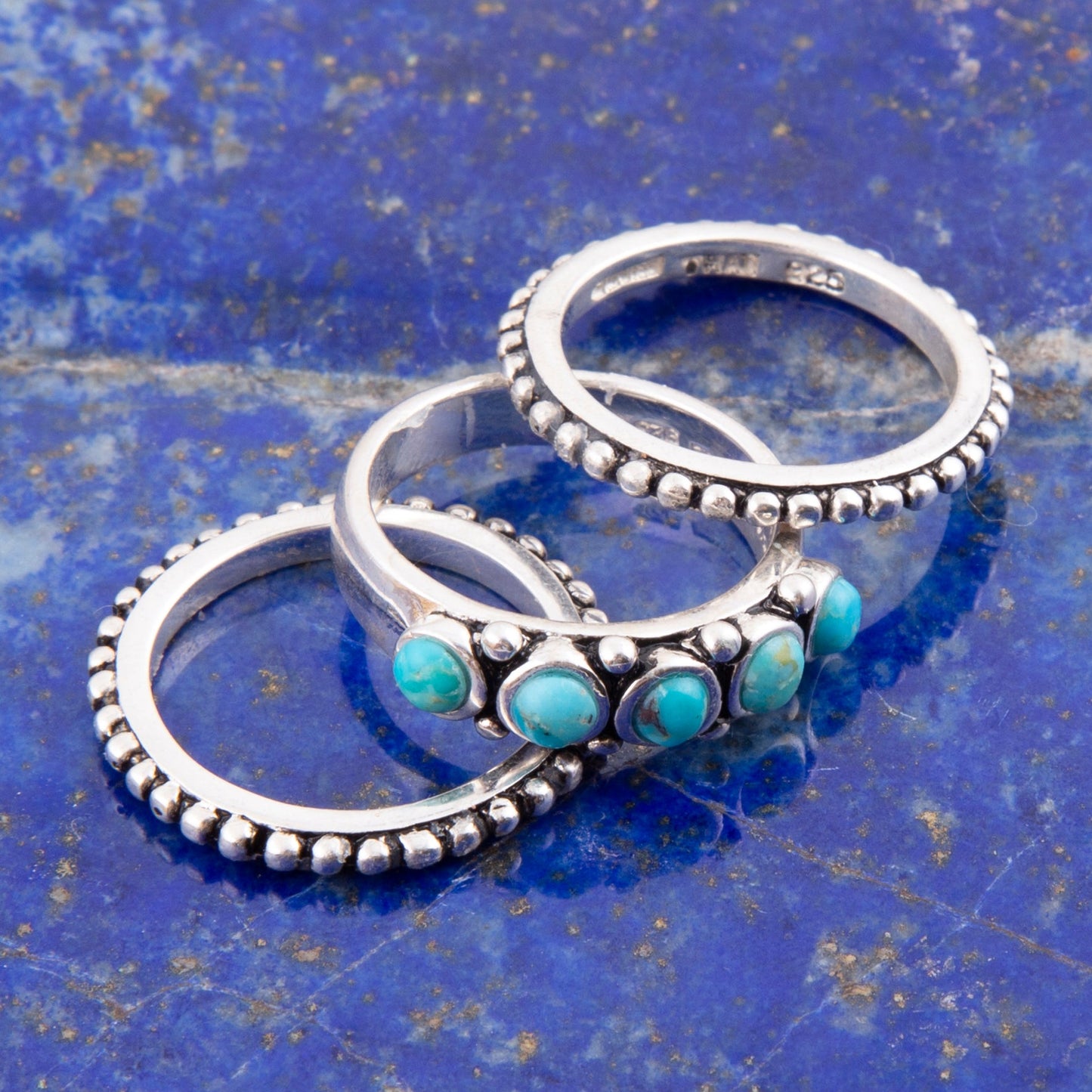 Three silver rings with turquoise stones on a blue textured surface