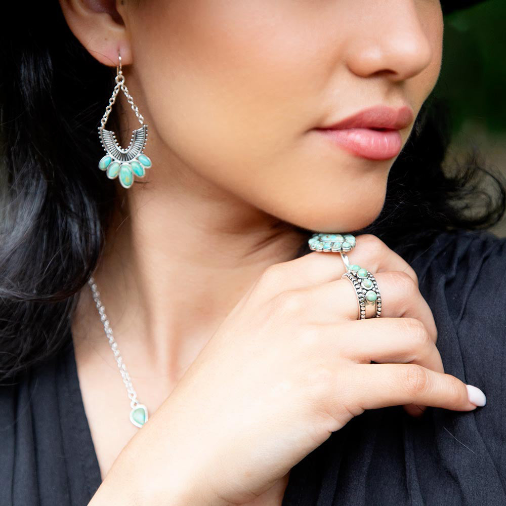 Close-up of a woman wearing turquoise jewelry including earrings, necklace, and rings.