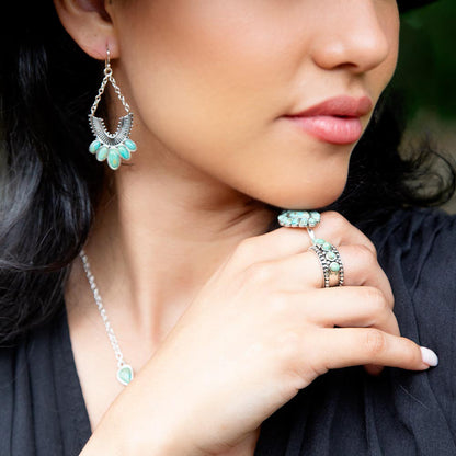 Close-up of a woman wearing turquoise jewelry including earrings, necklace, and rings.