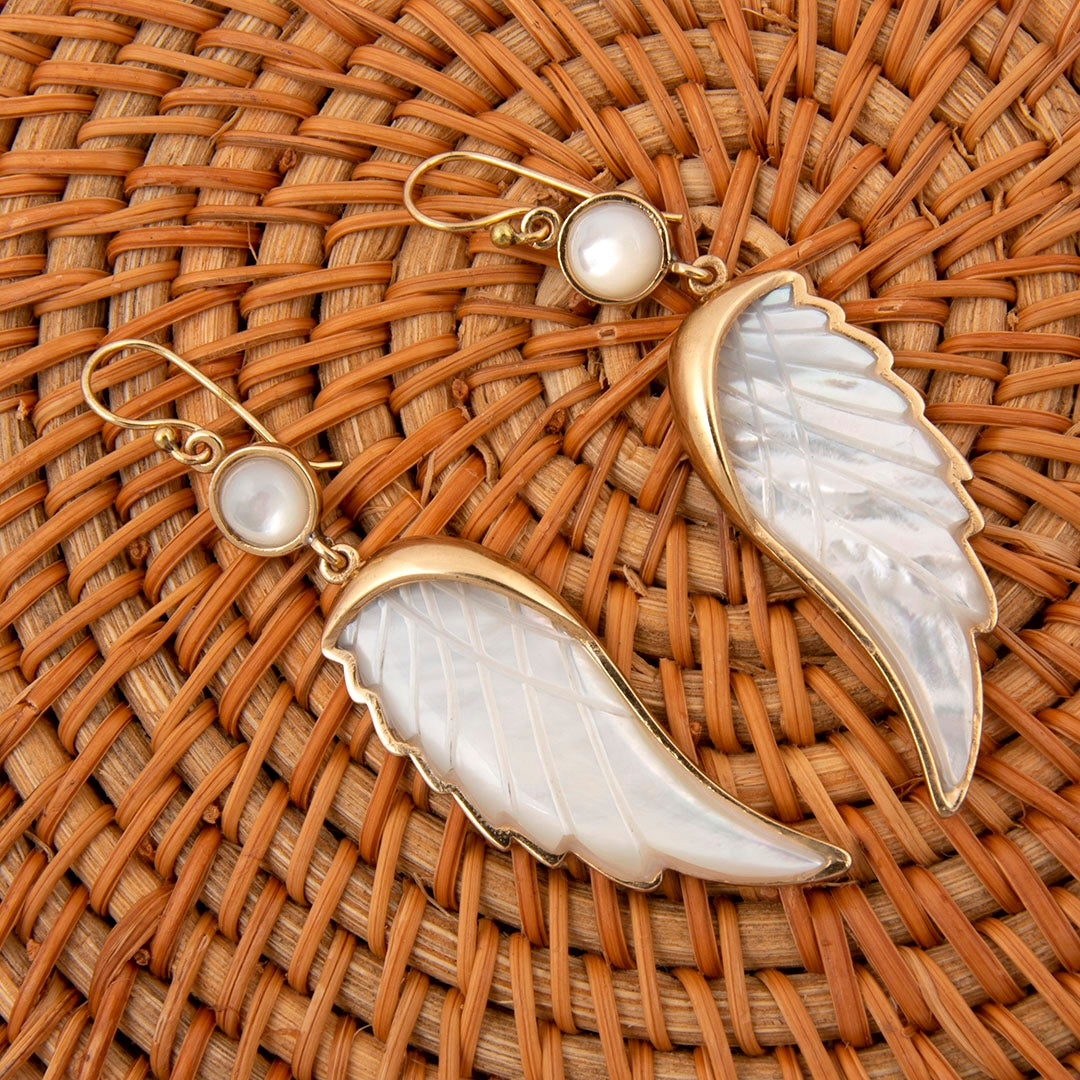 Gold and white wing-shaped earrings on a woven surface
