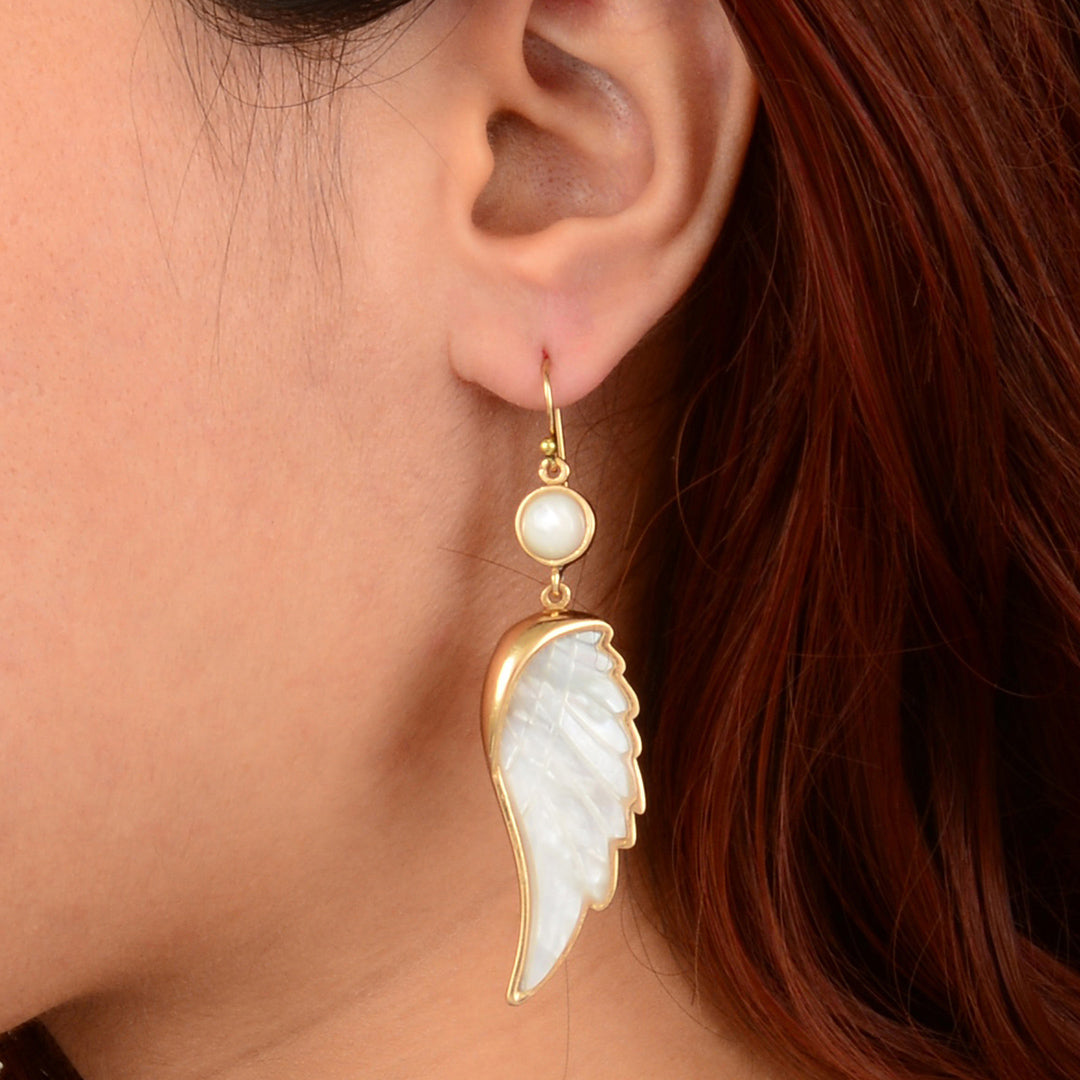 Close-up of a person wearing angel wing earrings with gold accents.