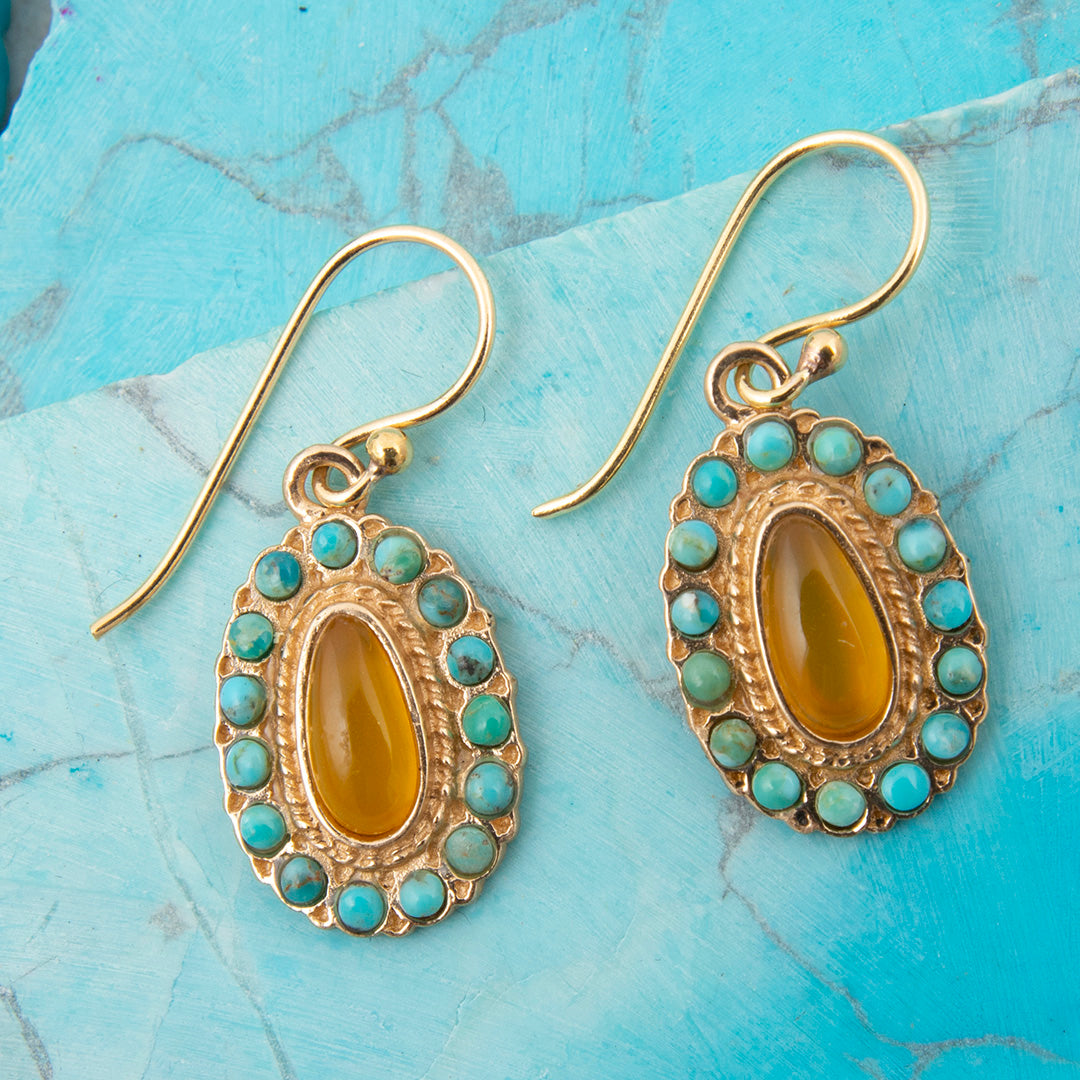 Gold earrings with yellow center stones and turquoise accents on a blue marble surface