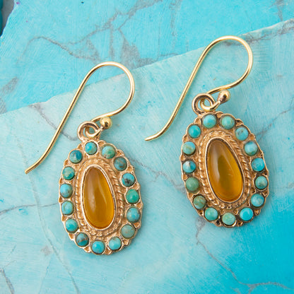 Gold earrings with yellow center stones and turquoise accents on a blue marble surface
