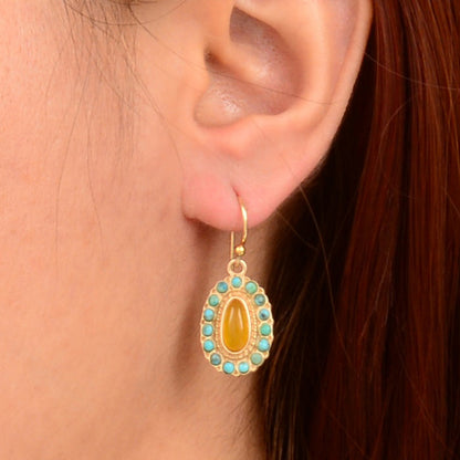Gold earring with a yellow center and turquoise stones worn by a person.