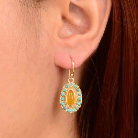 Gold earring with a yellow center and turquoise stones worn by a person.
