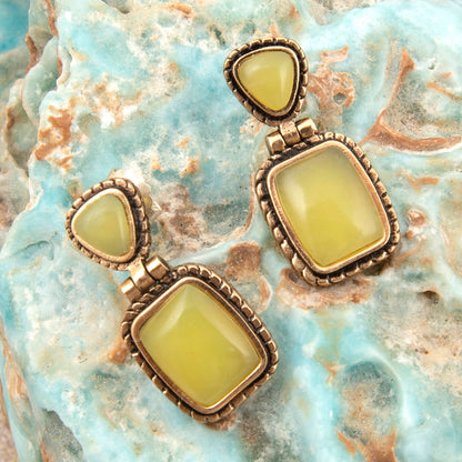 Pair of earrings with green stones on a textured stone surface