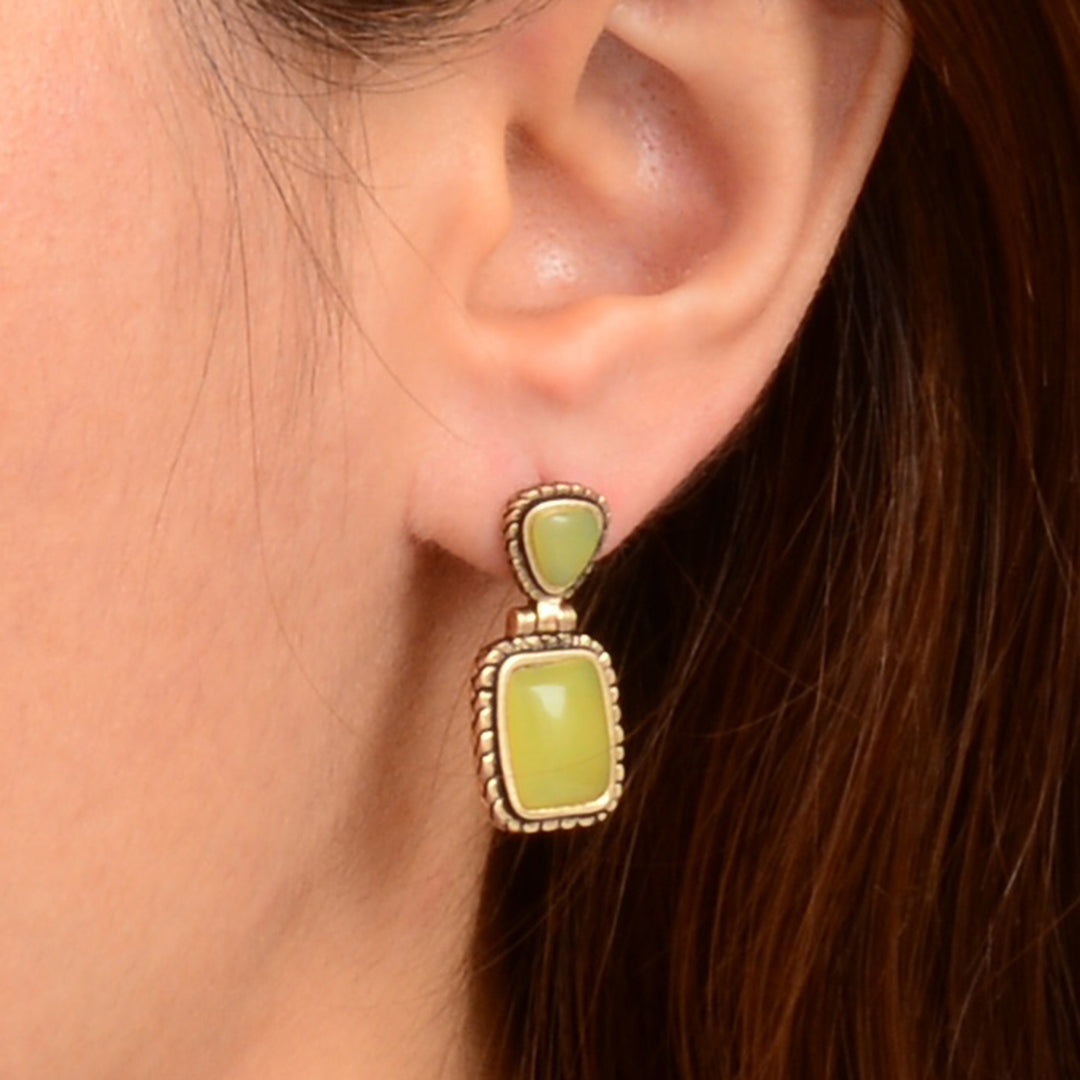 Close-up of a person wearing green earrings with gold accents.