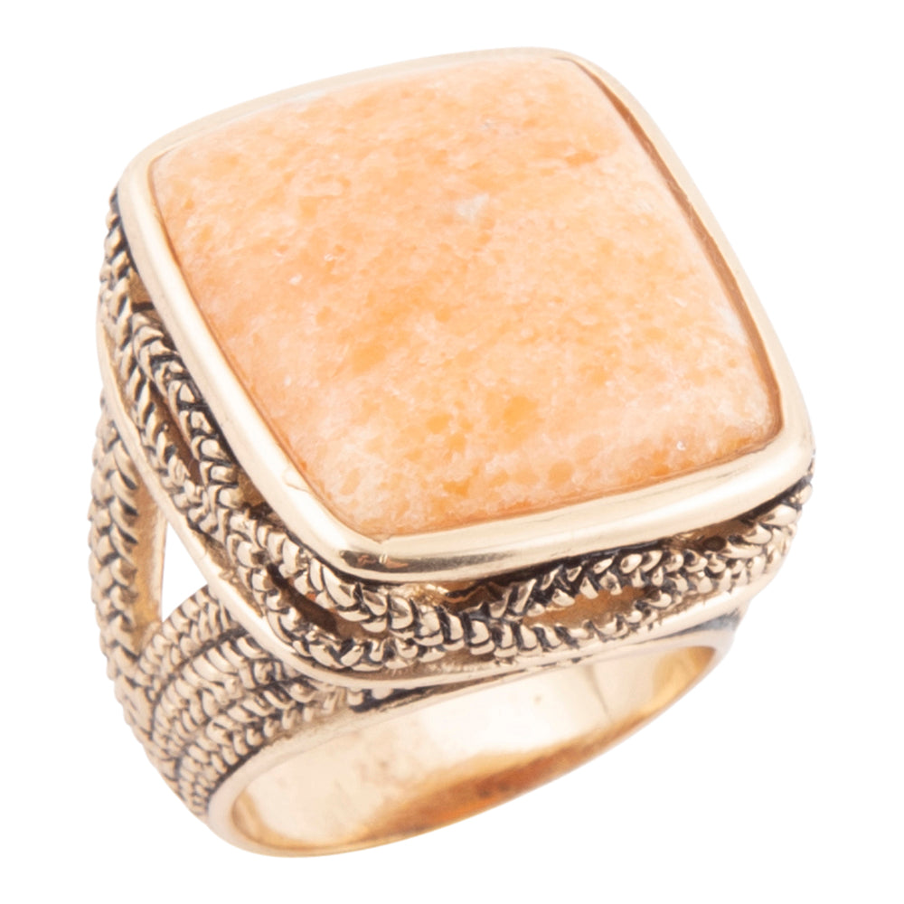 A square bezel-set ring featuring a textured, warm peach-orange stone, set in an ornate, braided gold-tone metal band with a polished gold inner band, shown against a plain white background.