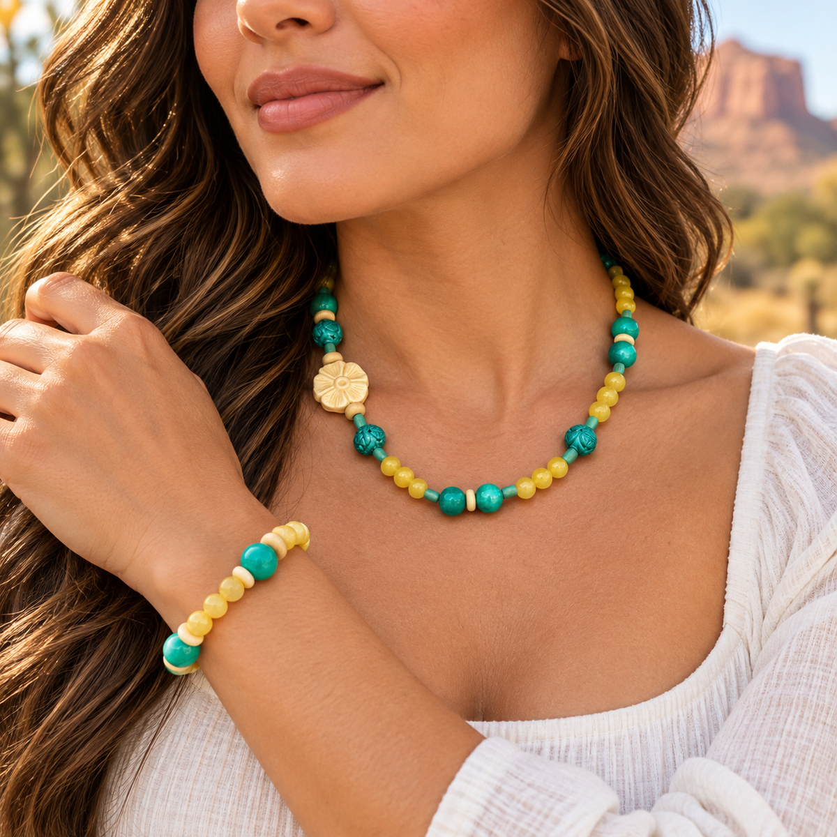 A woman wearing a matching beaded necklace and bracelet set in turquoise, yellow, and cream, with a gold clover charm on the necklace, set against a warm desert landscape background.