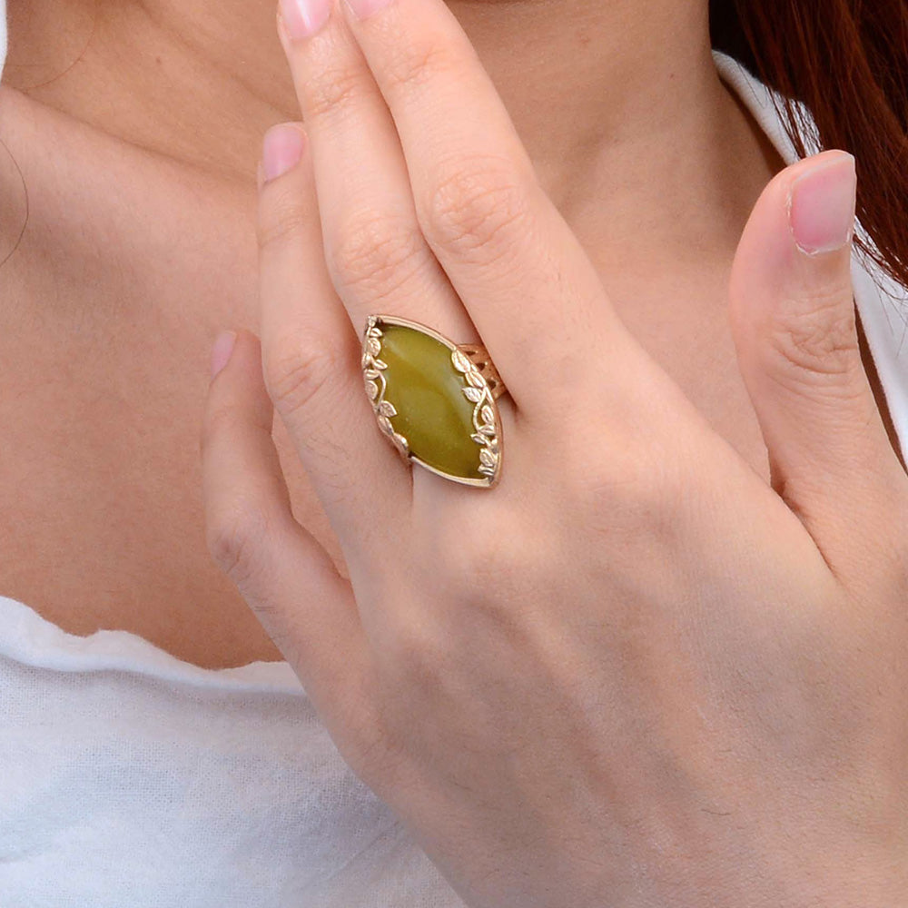 Hand wearing a green ring with gold detailing on a light background