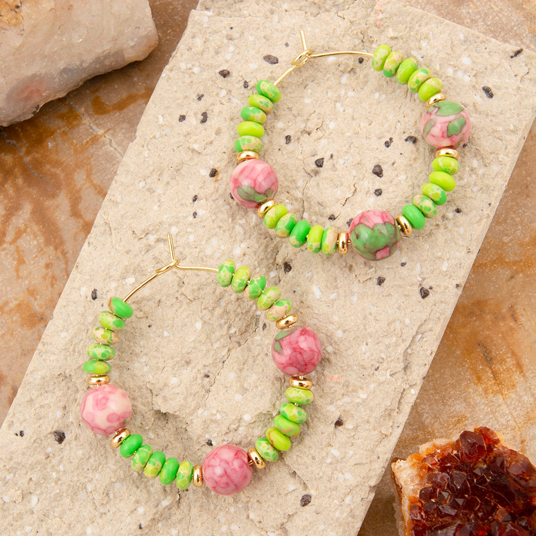 Green and pink beaded hoop earrings on a stone surface