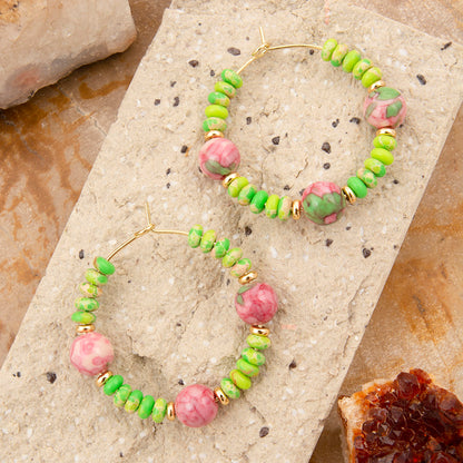 Green and pink beaded hoop earrings on a stone surface