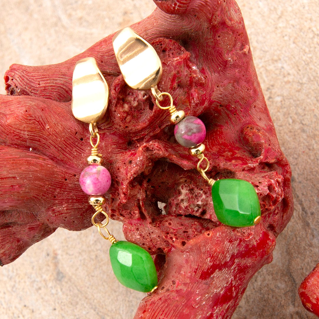 Gold earrings with pink and green beads on a red coral background
