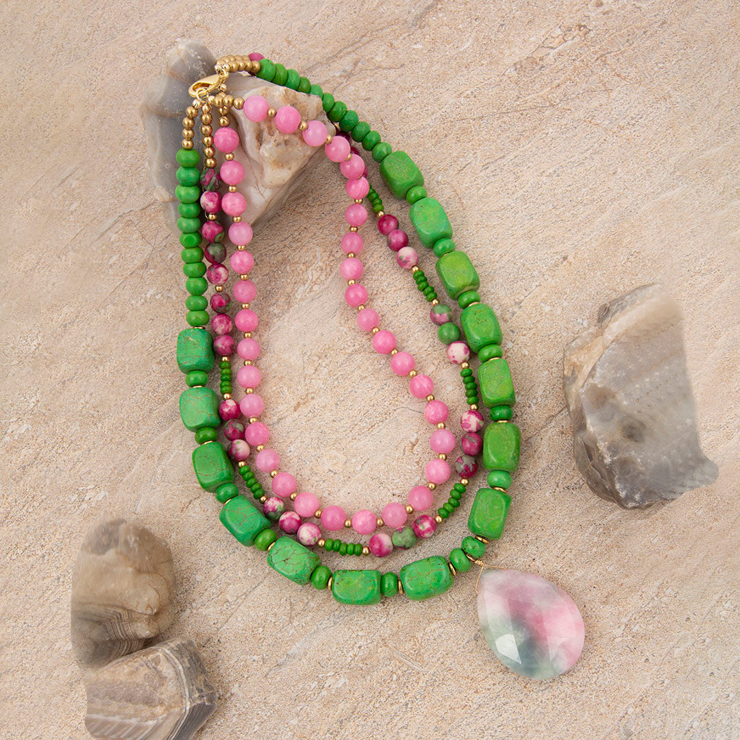 Green and pink beaded necklace on a sandy surface with stones