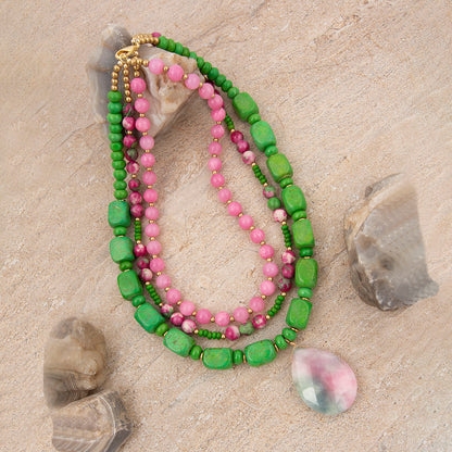 Green and pink beaded necklace on a sandy surface with stones