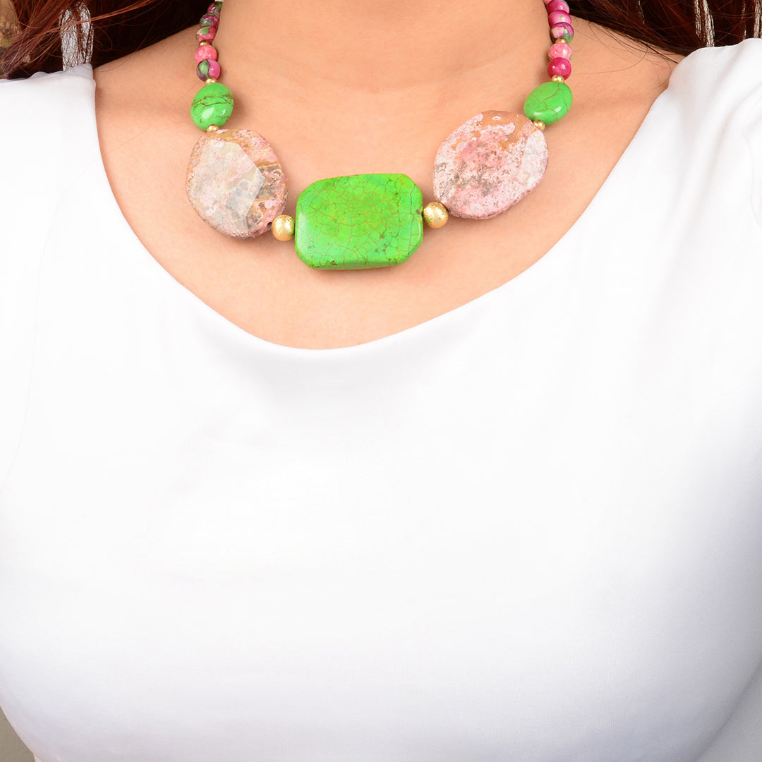 Necklace with green and pink beads worn by a person against a white background
