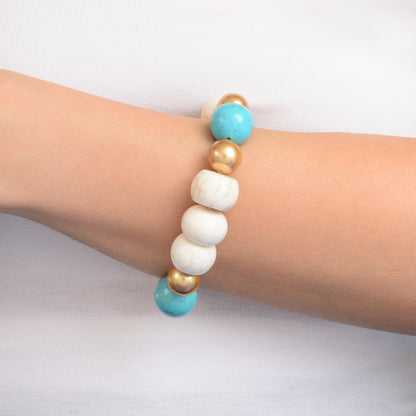 A beaded stretch bracelet worn on a person's wrist, featuring white marbled beads, gold metallic beads, and turquoise blue beads, set against a plain white background.