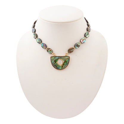 A necklace displayed on a white mannequin bust, featuring a strand of iridescent abalone shell beads and a large semicircular green abalone pendant with a gold-tone border and central white pearl.