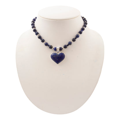 A beaded necklace with dark blue lapis lazuli stones and a heart-shaped pendant, displayed on a white jewelry bust against a white background.