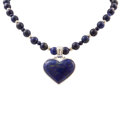 A beaded necklace featuring dark blue lapis lazuli stones and polished silver-toned spacer beads, with a heart-shaped lapis lazuli pendant in a silver bezel setting, shown against a plain white background.
