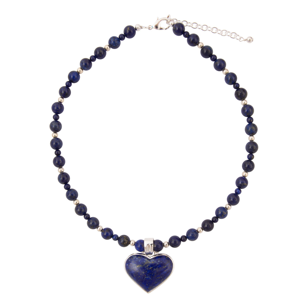 A beaded necklace featuring dark blue lapis lazuli stones separated by small silver spacer beads, with a polished heart-shaped lapis lazuli pendant set in silver at the center. The necklace is displayed on a clean white background.