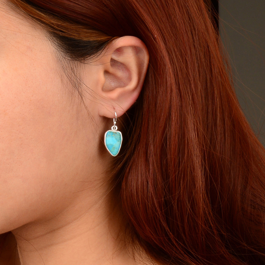Close-up of a person wearing a turquoise teardrop earring with red hair.