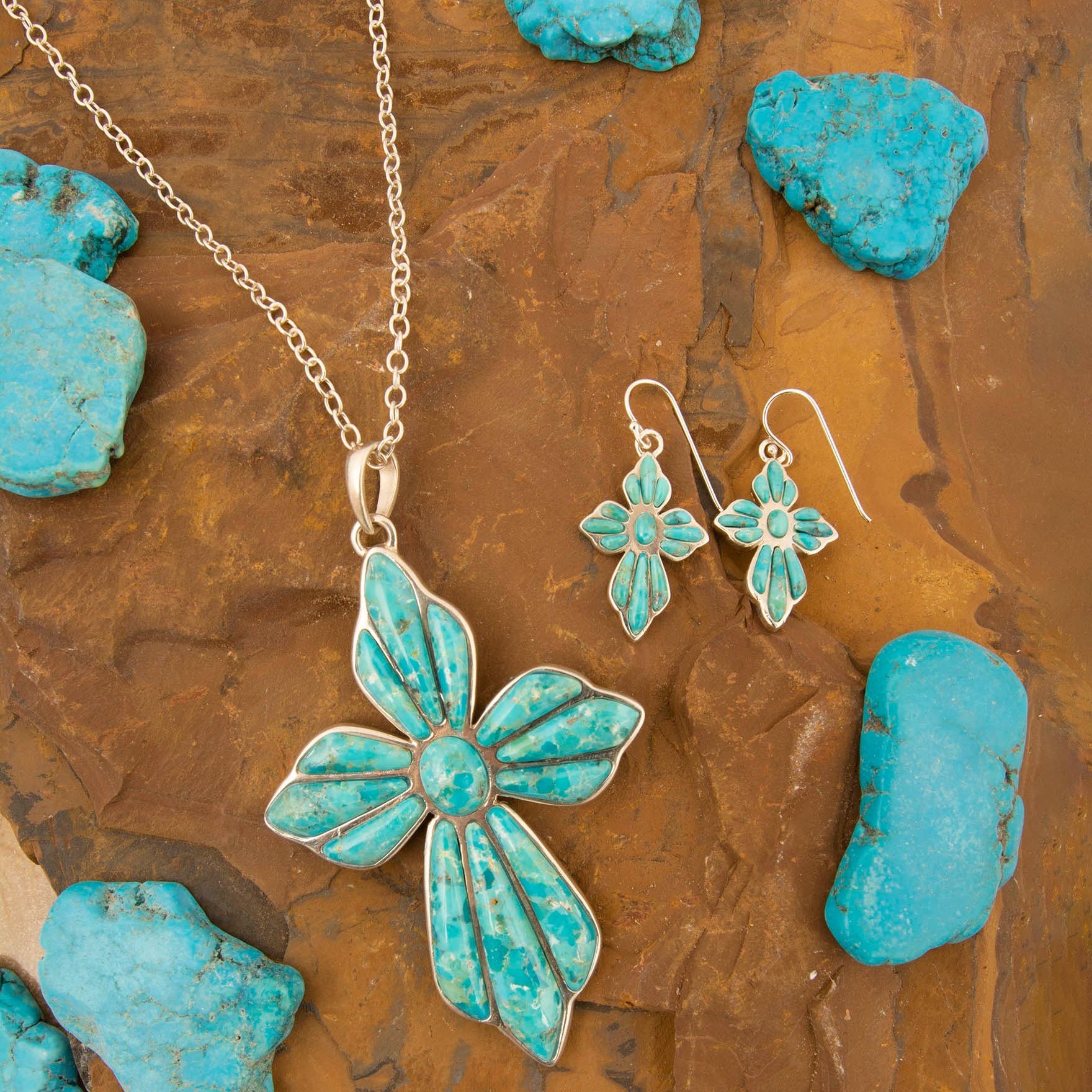 Turquoise butterfly necklace and earrings on a textured brown surface with turquoise stones.