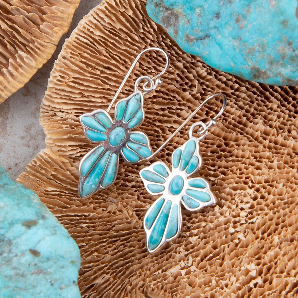 Turquoise butterfly earrings on a textured brown surface with turquoise stones.