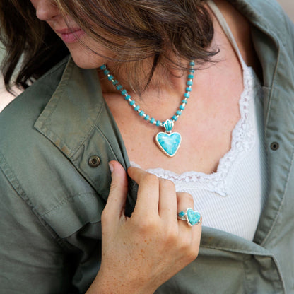 Person wearing a turquoise necklace and ring with a heart pendant.