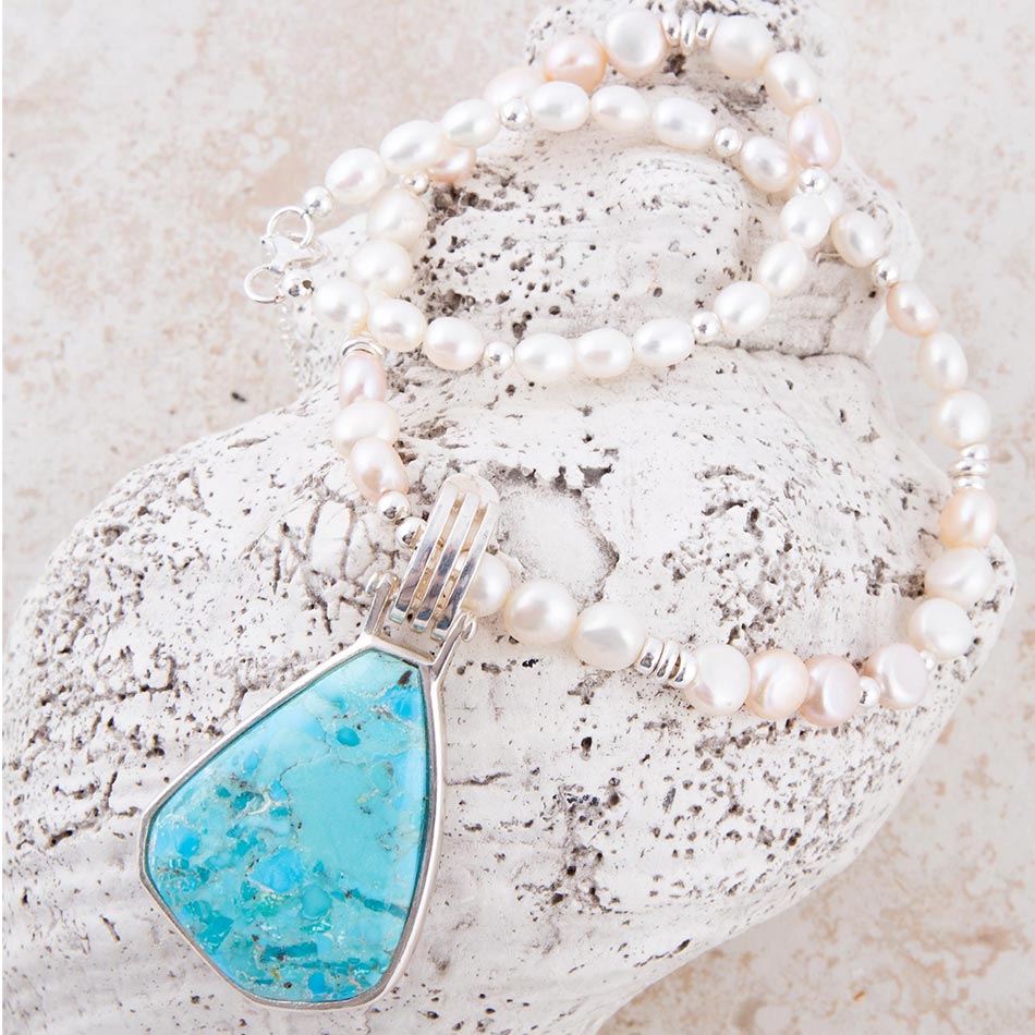 Pearl necklace with a turquoise pendant on a textured surface