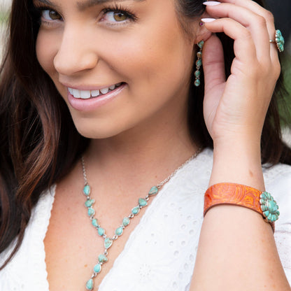 Woman wearing turquoise jewelry including earrings, necklace, and bracelet, with a blurred natural background.