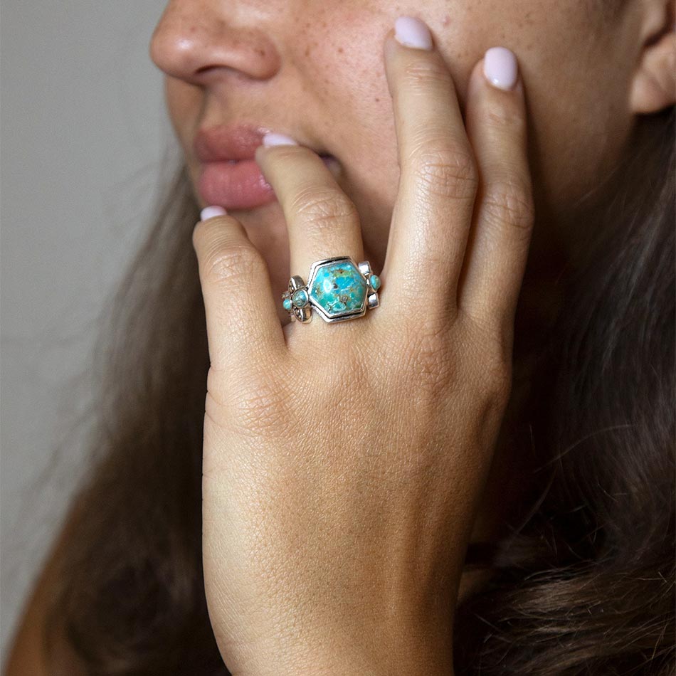 Close-up of a hand wearing a turquoise ring with a neutral background