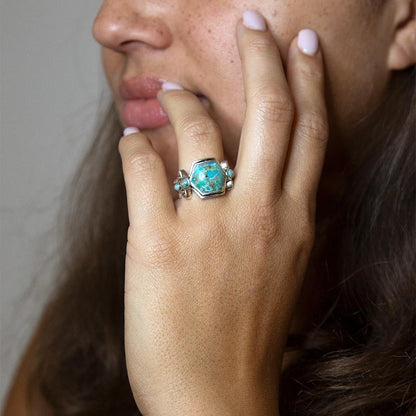 Close-up of a hand wearing a turquoise ring with a neutral background