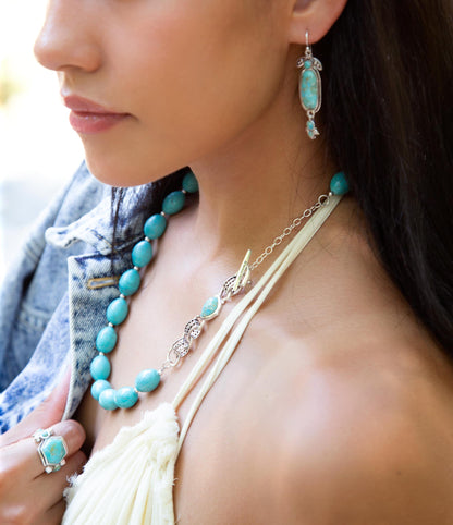 Close-up of a woman wearing turquoise jewelry including earrings, necklace, and ring.