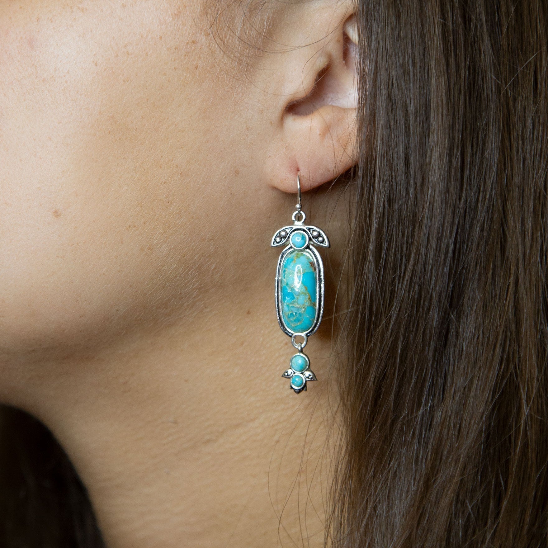 Turquoise earrings worn by a person with dark hair.